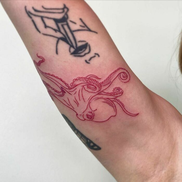 Red ink tattoo of an octopus on an arm, showcasing intricate linework.