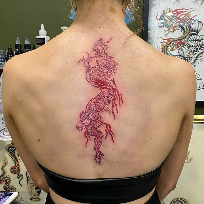 Red ink dragon tattoo on woman's back, showcasing intricate design and vivid color.