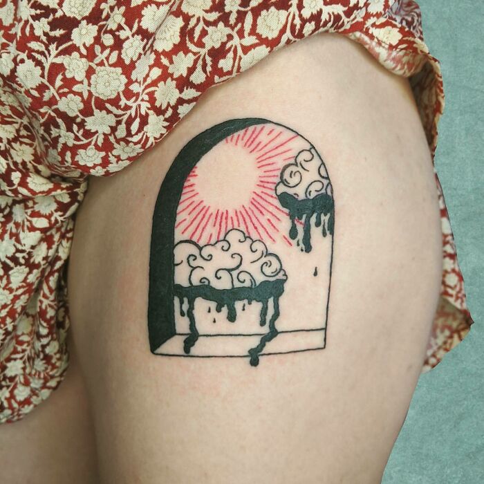 Red ink tattoo featuring a sunburst above abstract clouds on a person's thigh.