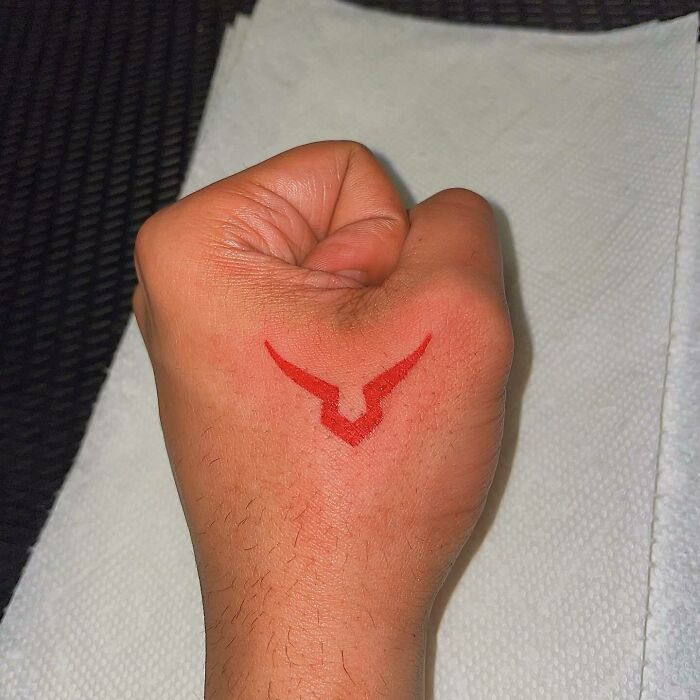 Red ink tattoo on hand featuring a minimalistic design.