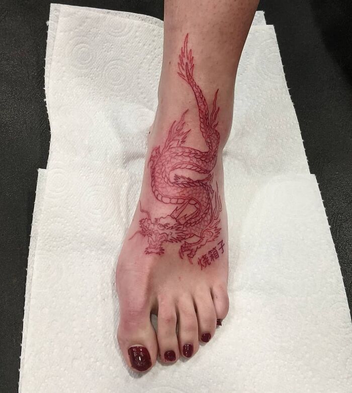 Red ink dragon tattoo on a foot, showcasing intricate details and bold design.