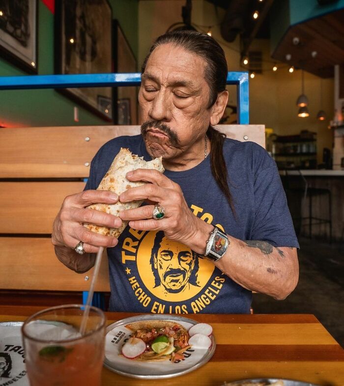 Celebrity enjoying a burrito at a restaurant table, wearing a graphic T-shirt.