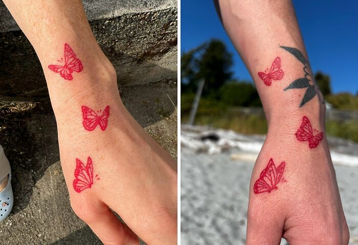 Red ink tattoos of butterflies on arms, showcasing intricate design and vibrant color in an outdoor setting.