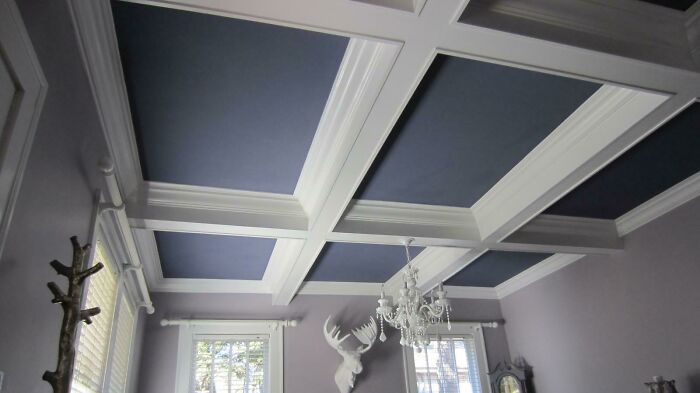 Ceiling decoration with blue panels and white beams in a creatively designed room, featuring a decorative chandelier and wall art.