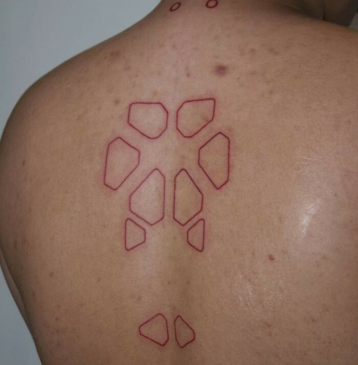 Geometric red ink tattoo design on a person's back.