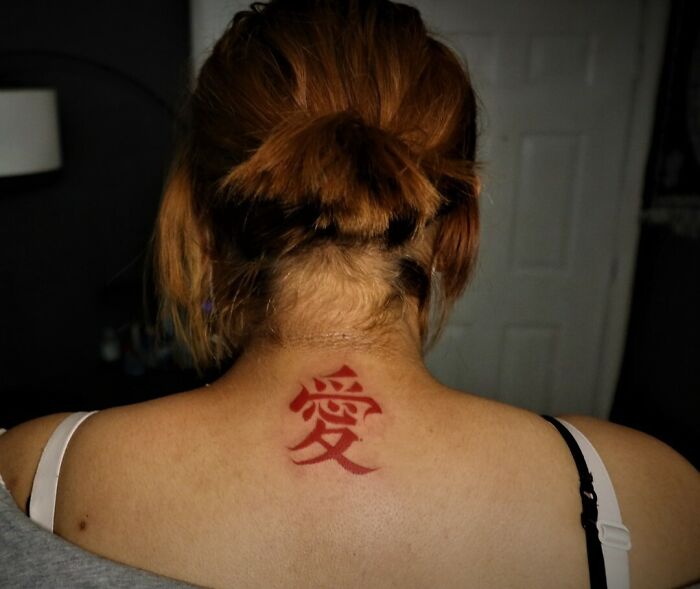 Red ink tattoo on upper back depicting a Chinese character, with hair tied up, highlighting tattoo design.