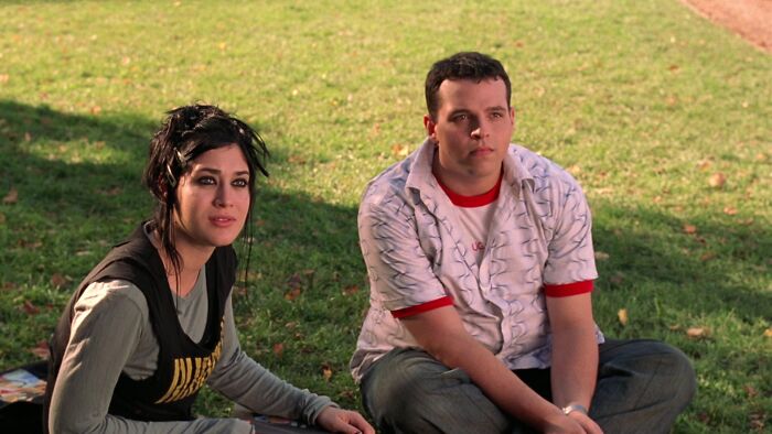 Two people sitting on grass, representing iconic best friend duos, gaze off into the distance.