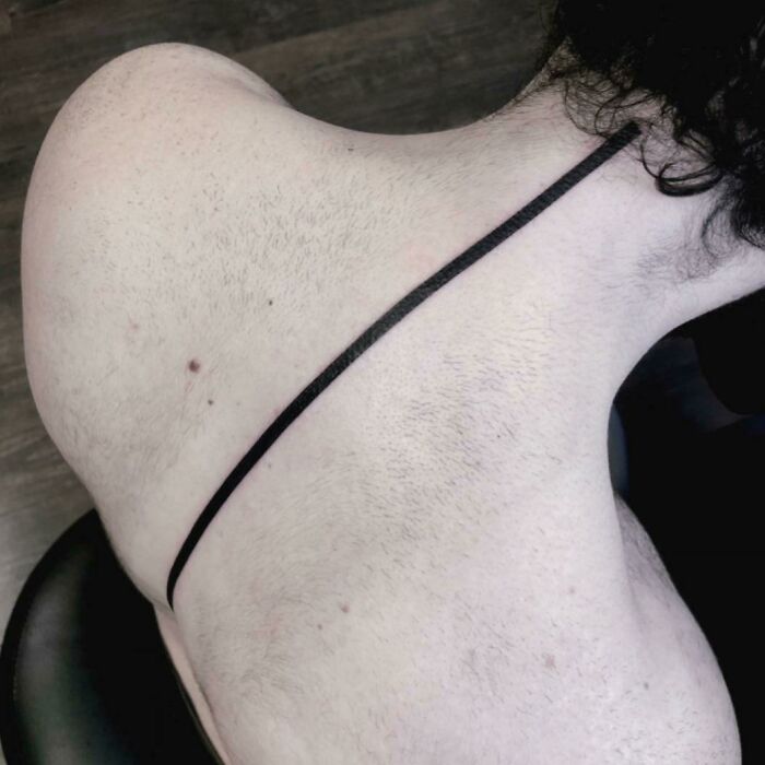 Minimalist spine tattoo with a bold black line running down the back.