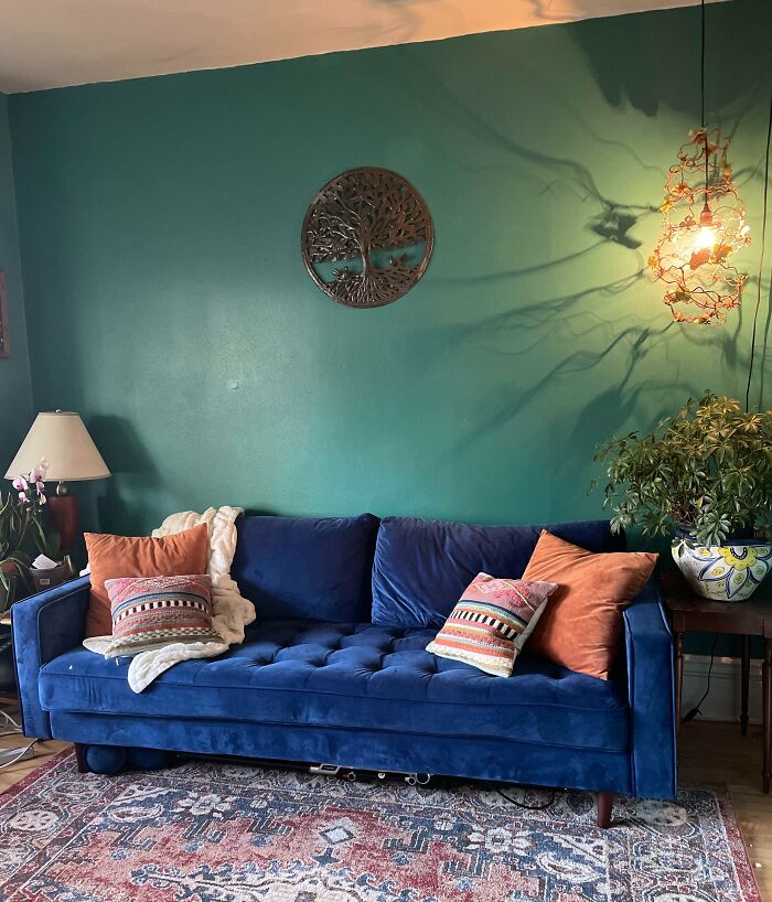 Blue sofa with colorful pillows against a teal accent wall, featuring creative home decoration elements.
