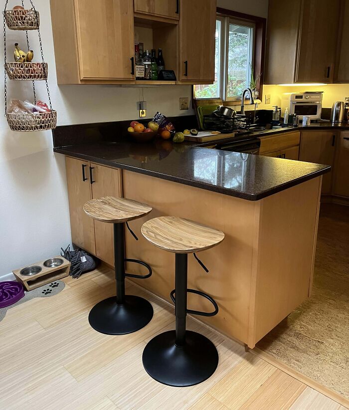 Creative kitchen design with two modern bar stools at a wooden counter, fruit on top, and hanging baskets.
