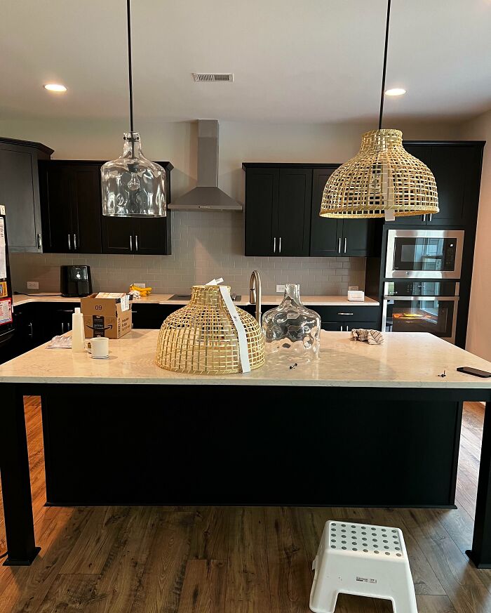 Kitchen island with wicker lampshades and glass vases, black cabinets, ideal for decoration inspiration.