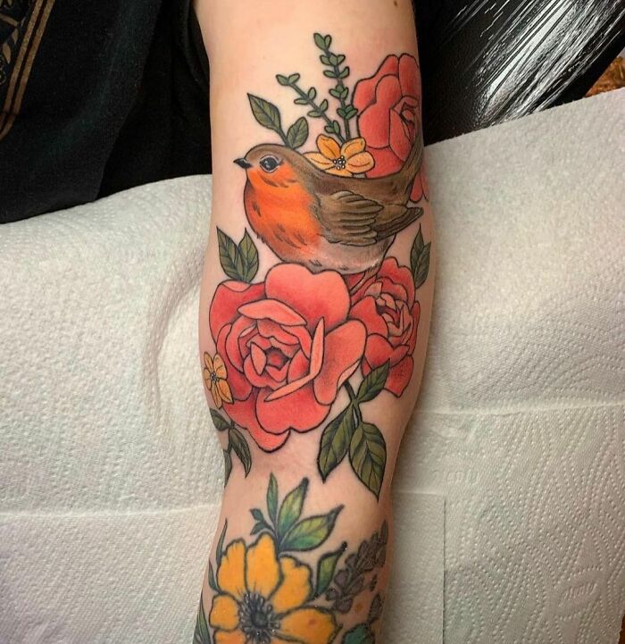 Nature tattoo of a bird perched on red roses and orange flowers, showcasing vibrant colors and intricate design.