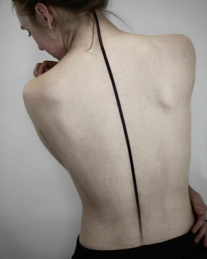 Elegant spine tattoo with a minimalistic black line design on a woman's back.