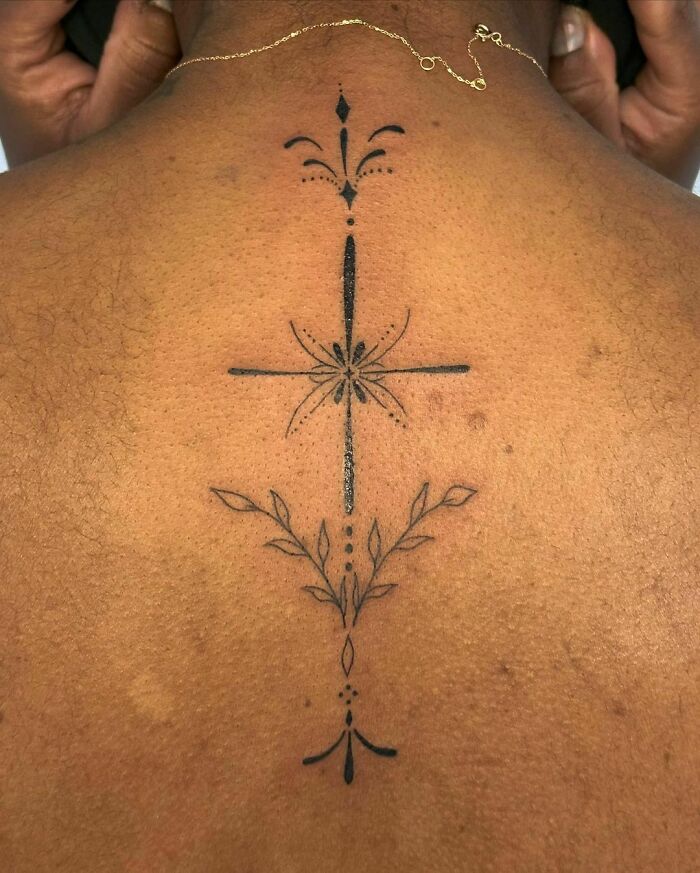 Elegant spine tattoo with floral and geometric design on person's back.