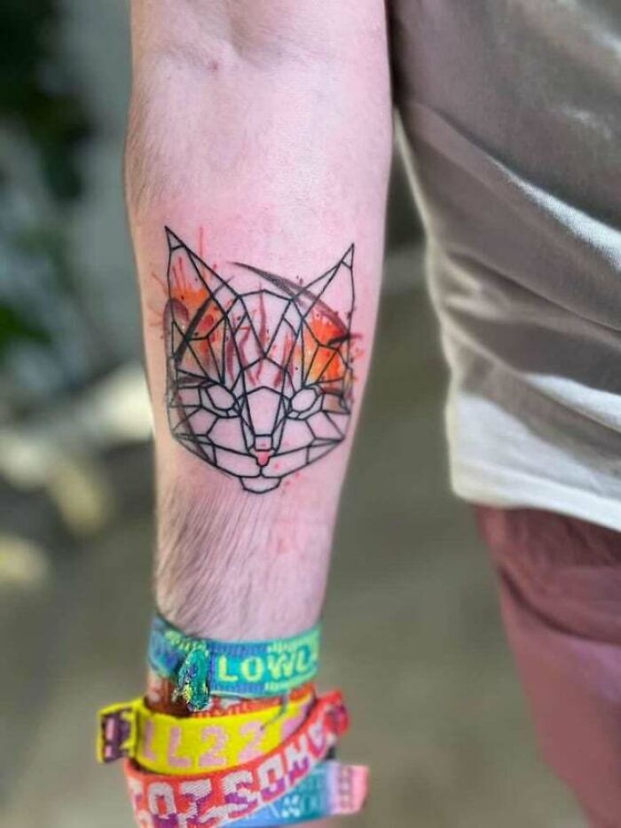 Geometric animal tattoo with orange accents on forearm, surrounded by colorful wristbands.