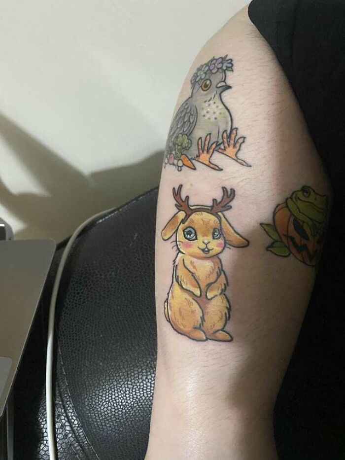 Colorful animal tattoos, featuring a bird with flowers and a cute antlered rabbit, on a person's arm.