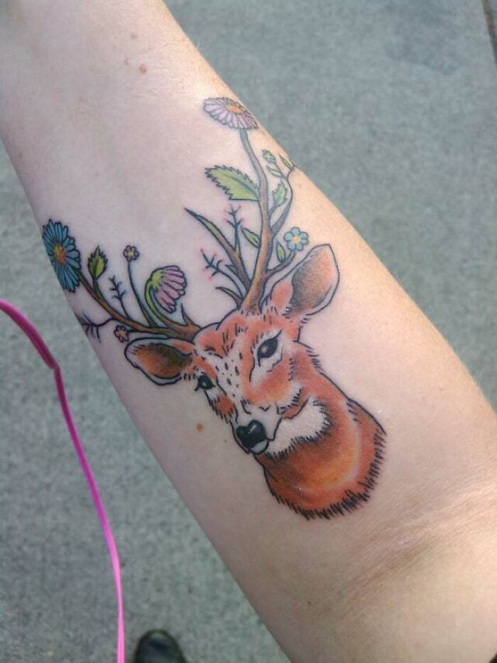Deer tattoo with floral antlers on forearm, showcasing vibrant animal tattoo art.