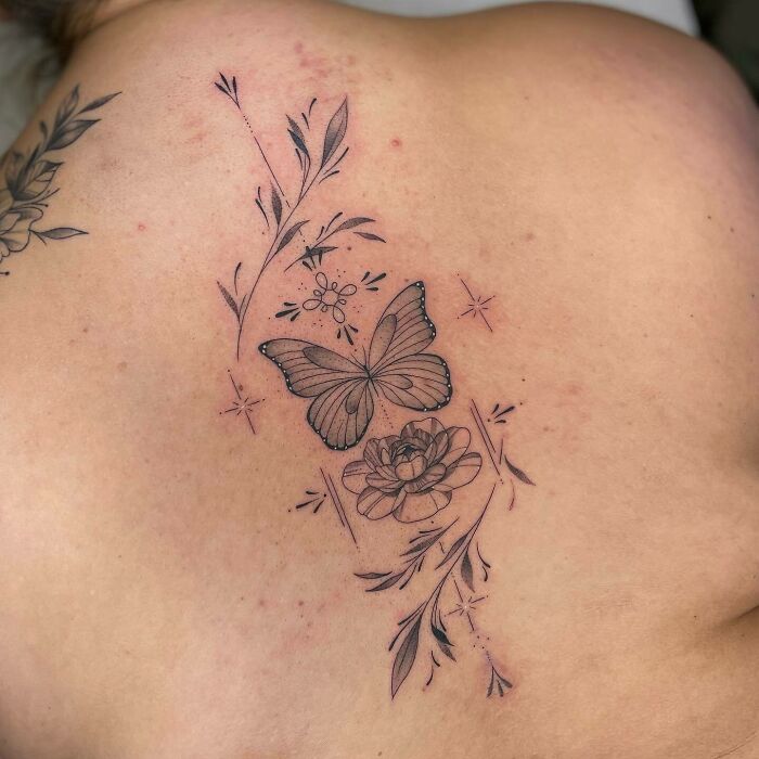 Elegant spine tattoo featuring a butterfly and floral design on a person's back.