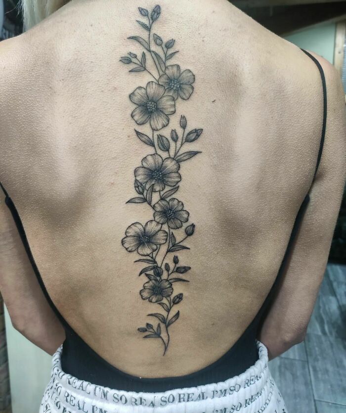 Elegant spine tattoo featuring a vertical floral design on a person's back, showcasing intricate artistry and detail.