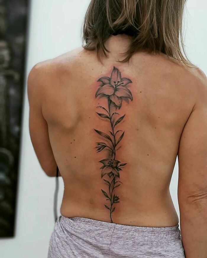 Person showcasing an elegant floral spine tattoo design on their back.