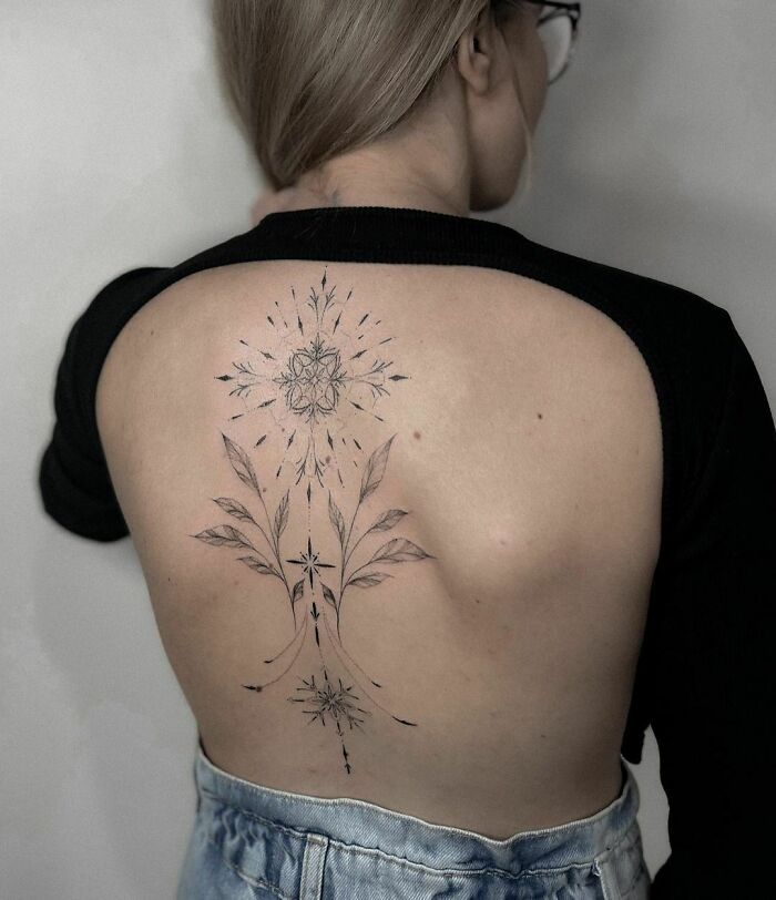 Elegant spine tattoo featuring floral and geometric designs on a person's back, showcasing intricate ink art.