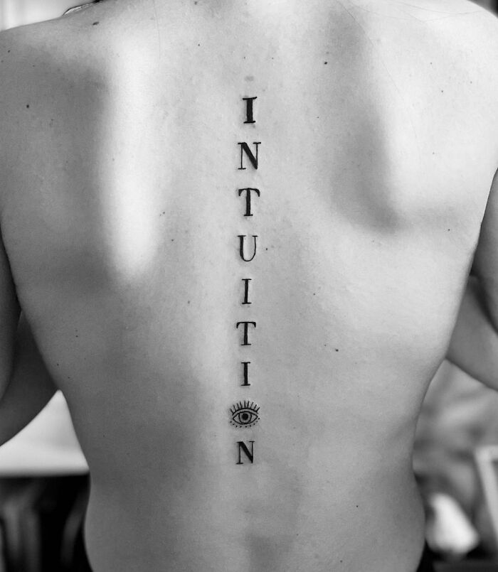 Spine tattoo reading "INTUITION" with an eye symbol, showcasing an elegant design for men and women.