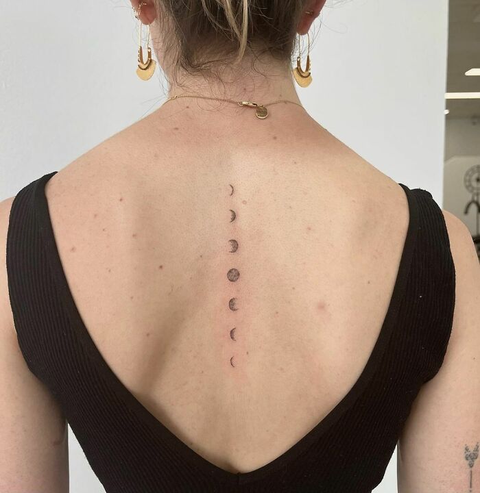 Elegant spine tattoo featuring moon phases on a woman's back, accented by a black dress.