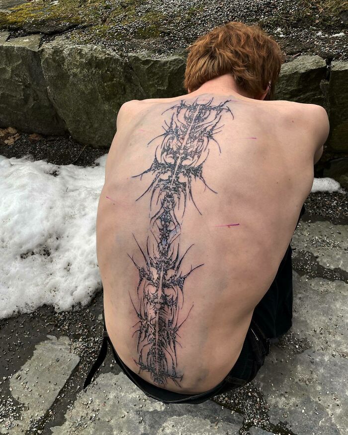 Elegant spine tattoo design with intricate patterns on a person's back, seated outdoors on a snowy day.