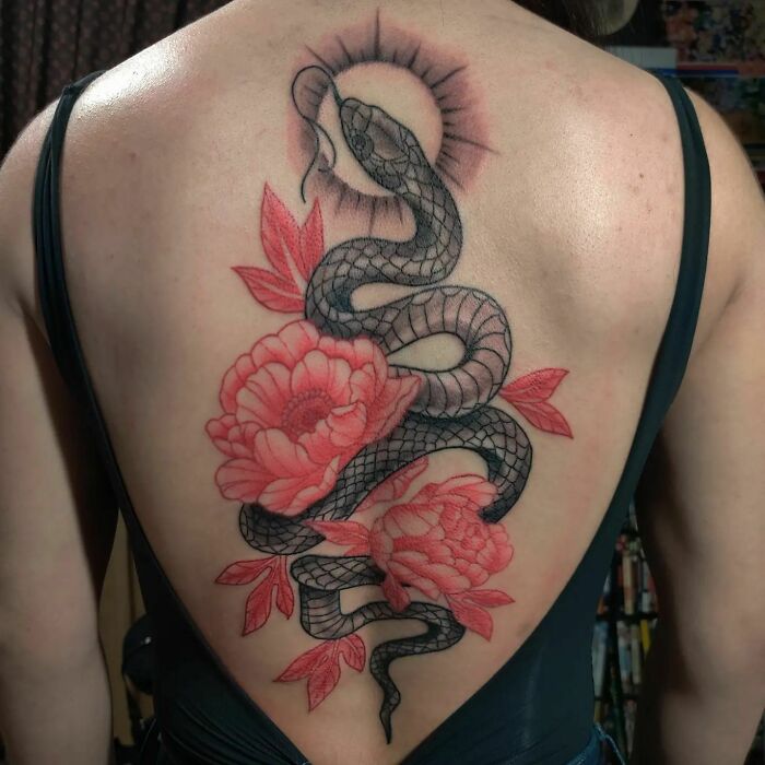 Large snake and two red flowers tattoo on woman’s back