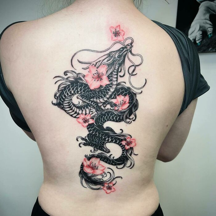 Elegant spine tattoo featuring a black dragon intertwined with pink flowers on a woman's back.
