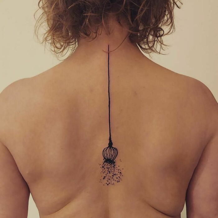 Elegant spine tattoo featuring a delicate line and floral design on a woman's back.