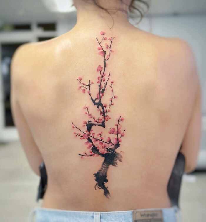 Cherry blossom spine tattoo with pink petals on back, showcasing intricate design.