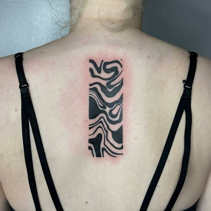 Abstract spine tattoo with black and white wavy lines on a person's back.