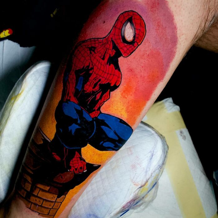 Marvel tattoo of Spider-Man perched on a ledge with a vibrant orange background.