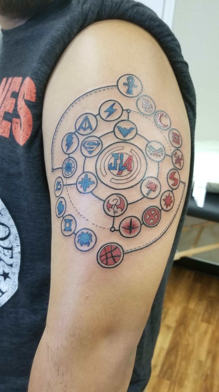 Arm with a colorful Marvel tattoo featuring superhero logos interconnected in a circular pattern.