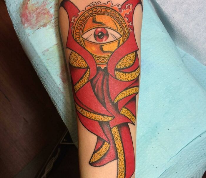 Marvel tattoo featuring a red and gold design with an eye on a forearm, showcasing vibrant superhero themes.