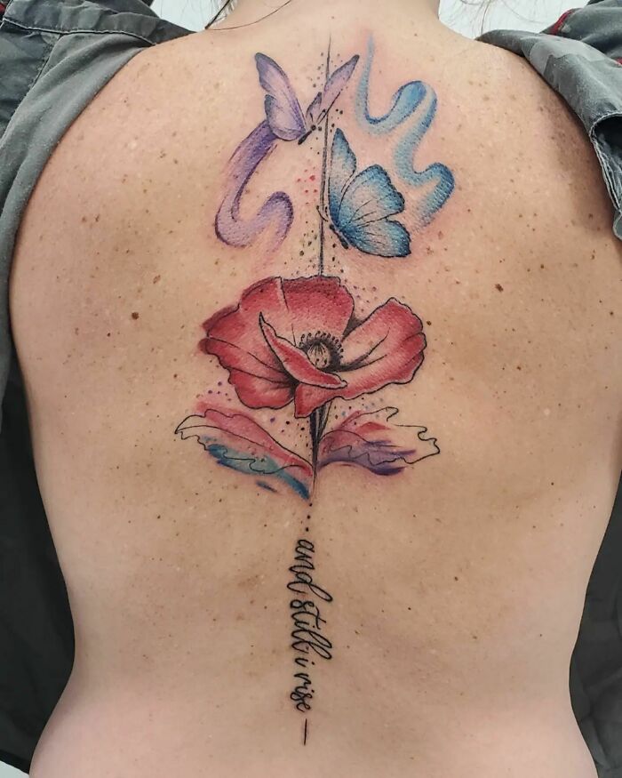 Colorful spine tattoo featuring a red flower, blue butterflies, and script, showcasing elegant designs for men and women.