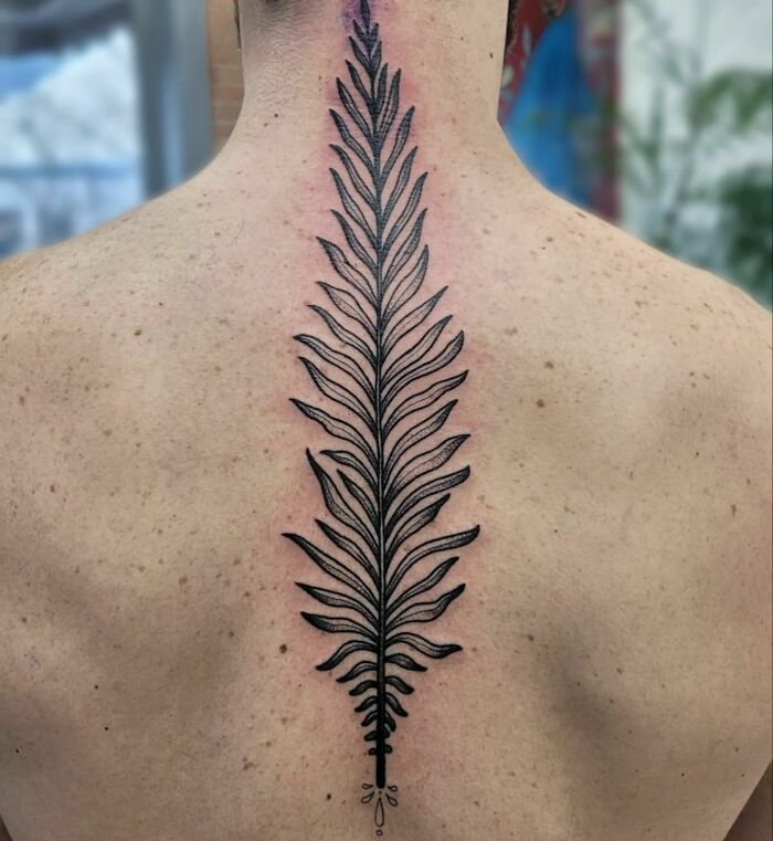 Elegant spine tattoo design featuring a symmetrical leaf pattern on a person's back.