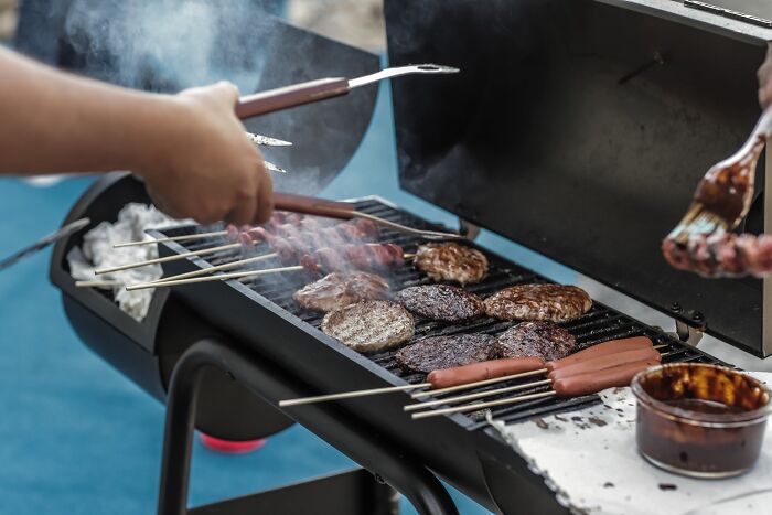 person frying meat and sausages on the barbecue