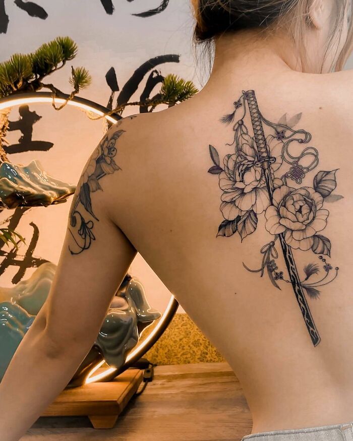 Elegant spine tattoo featuring floral and sword design on a woman's back.