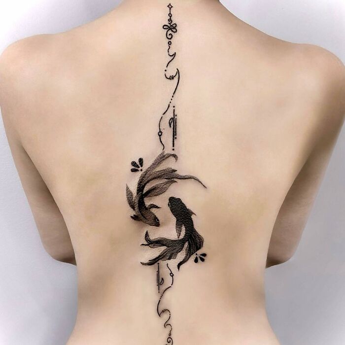 Ornate spine tattoo featuring artistic black fish and floral designs on a person's back.