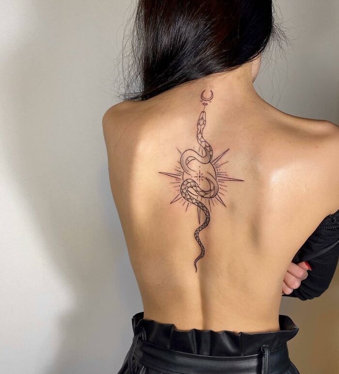 Woman showcasing an elegant spine tattoo featuring a snake and celestial design.