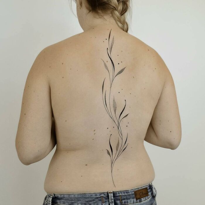 Minimalist spine tattoo with delicate leaves on a woman's back, showcasing elegant body art.