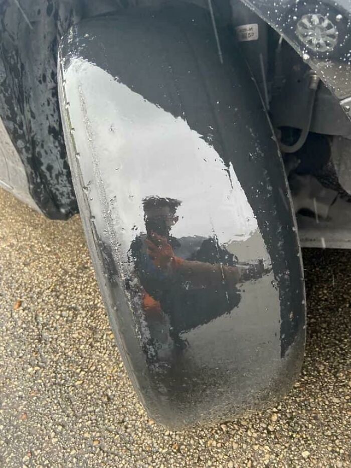 Man taking a picture of car tire and see's his reflection 