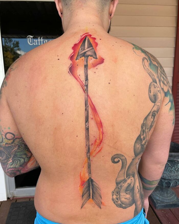 Arrow spine tattoo design with vibrant colors on a person's back, showcasing elegant tattoo artistry.