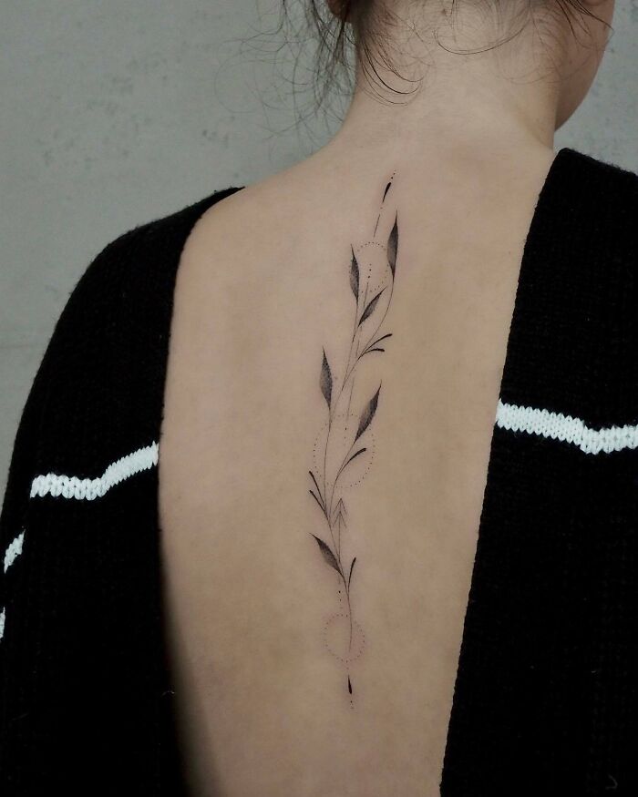 Elegant spine tattoo featuring a delicate leaf design on a woman's back.