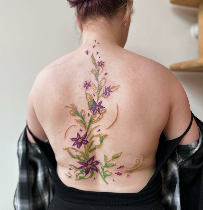 Elegant spine tattoo with purple and green floral design on a woman's back.