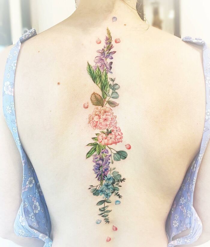 Different types of flowers and leaves along the spine tattoo