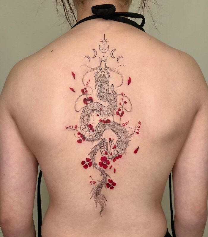 Elegant spine tattoo with dragon and floral details on woman’s back.