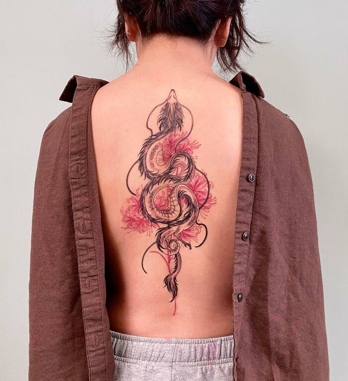 Elegant spine tattoo design featuring a black and red floral motif on a person's back, with a brown shirt partially revealing the tattoo.